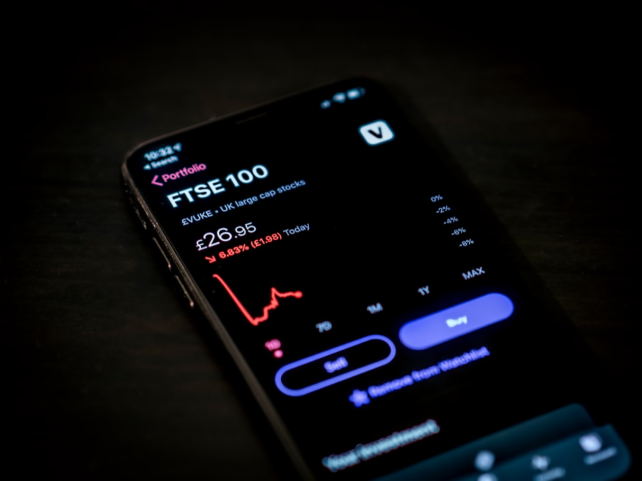 a black smartphone screen showing a falling stock market stat of an FTSE 100